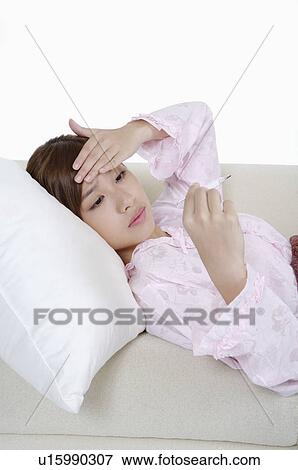 Young woman lying on sofa with hand on head and using thermometer View Large Photo Image Stock Photo - Young woman lying on sofa with hand on head and using thermometer. Fotosearch