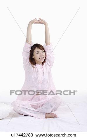 Young woman sitting on bed and stretching with smile View Large Photo Image Stock Image - Young woman sitting on bed and stretching with smile. Fotosearch