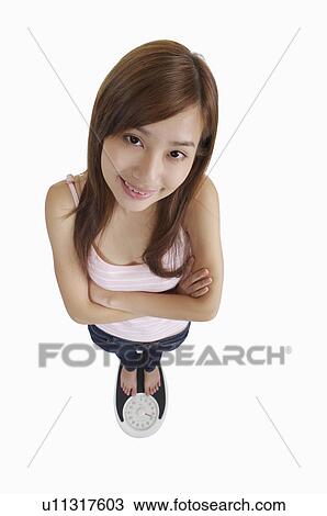 Young woman standing on weight scale and smiling with arms crossed View Large Photo Image Stock Image - Young woman standing on weight scale and smiling with arms crossed. Fotosearch