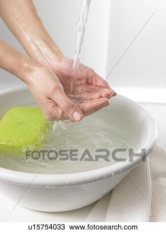Stock Image - Water is running through hands into a washbowl. Fotosearch