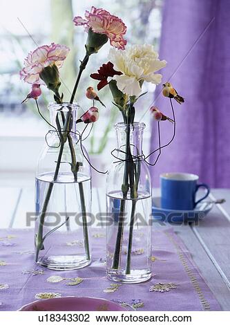 Stock Image - Carnations in glass bottles decorated with artificial birds. Fotosearch