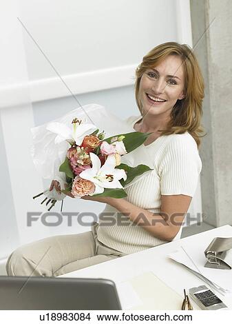 Picture - Woman with a bouquet sitting on her desk. Fotosearch