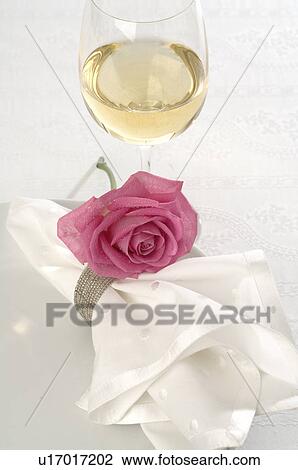 Stock Image - A glass of white wine and a napkin decorated with a pink rose blossom. Fotosearch
