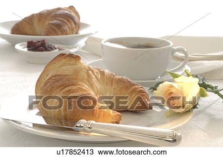 Stock Image - Place setting with a croissant and a white rose blossom. Fotosearch