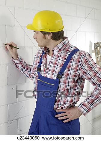 Stock Image - Construction worker is marking with a pencil on the wall. Fotosearch