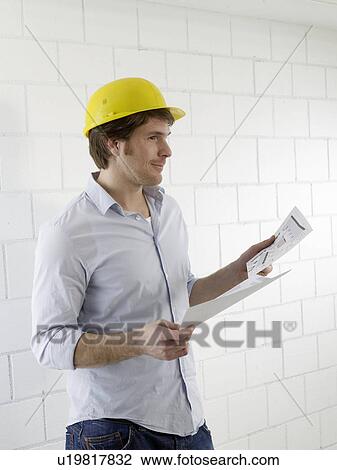 Man wearing a helmet with construction plans View Large Photo Image Stock Image - Man wearing a helmet with construction plans. Fotosearch