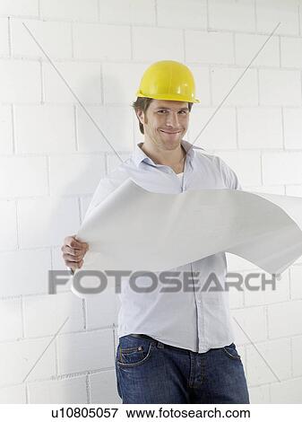 Stock Photo - Man wearing helmet with construction plans. Fotosearch