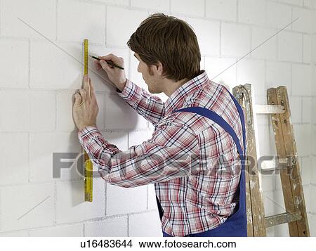 Picture - Man wearing work wear is marking on wall. Fotosearch