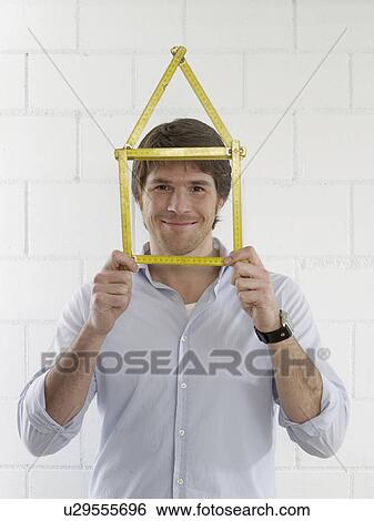 Stock Photograph - Man with a folding rule looking like a house. Fotosearch