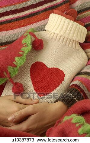 Stock Image - Hot water bottle in a beige overcoat with red heart. Fotosearch