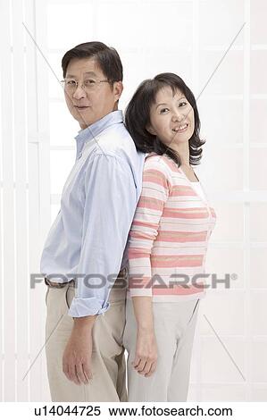 Stock Photography - Couple, Couple standing of back to back and looking at the camera with smile. Fotosearch