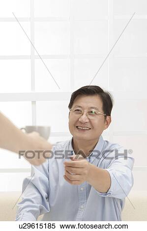 Stock Photography - Couple, Husband reaching hand to take a cup of tea from wife and smiling. Fotosearch