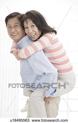 Stock Image - Couple, Wife on husband's back and looking at the camera with smile. Fotosearch