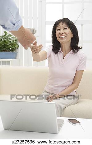 Stock Photograph - Couple, Woman sitting on sofa, reaching hand and smiling happily. Fotosearch