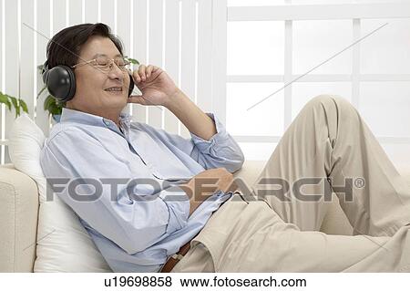 Stock Photo - Husband, Man lying on sofa and listening music with smile. Fotosearch