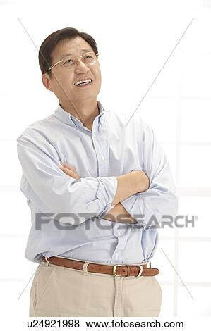 Stock Photo - Husband, Man standing with arms crossed and looking up with smile. Fotosearch