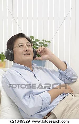 Stock Photo - Man lying on sofa and listening music with smile. Fotosearch