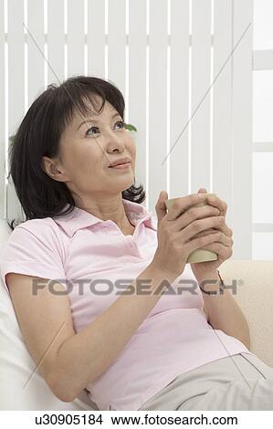 Wife. Woman holding a cup and looking up with smile View Large Photo Image Picture - Wife. Woman holding a cup and looking up with smile. Fotosearch