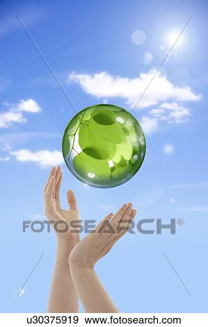 Stock Photo - Lohas, Environmental Conservation, Digitally generated image of human hands with a sphere with green leaves. Fotosearch