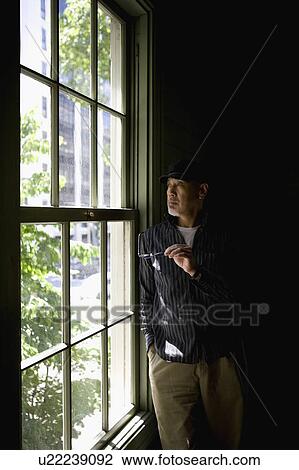 Stock Image - Senior man standing by window. Fotosearch