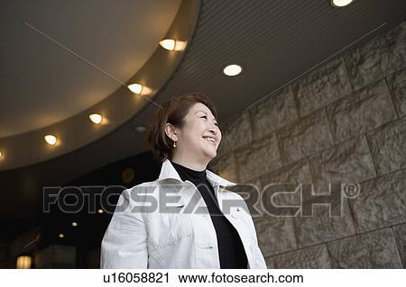 Stock Image - Senior woman standing in front of building. Fotosearch