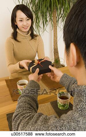 Stock Photo - Young woman giving Valentine's Day gift to young man. Fotosearch