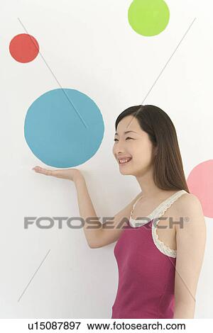 Stock Photo - Portrait of a Young Woman Posing in front of Polka Dots of Wall Paper, Side View. Fotosearch