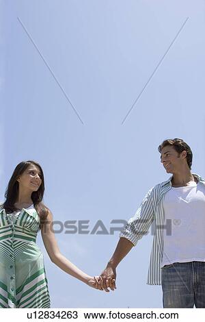 Stock Image - Young adult couple holding hands, Low Angle View, Copy Space. Fotosearch