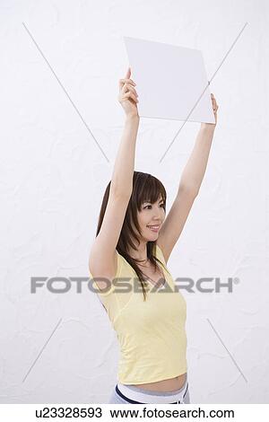 Stock Image - Young woman holding a white board, smiling, side view. Fotosearch