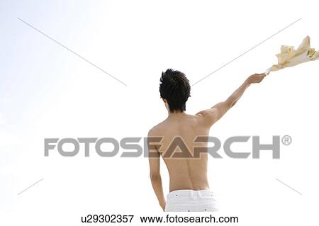 Stock Photo - Back figure of a young man at the beach with his shirt off. Fotosearch