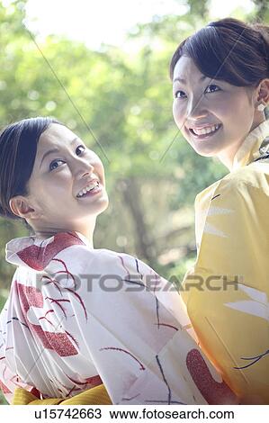 Stock Image - Back figure of smiling young women putting on a yukata. Fotosearch