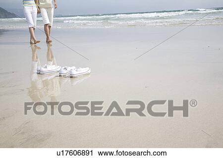 Stock Image - Foot of couple and shoes at the beach. Fotosearch