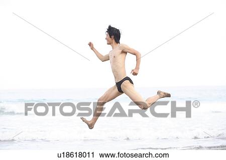 Stock Image - Happy young man jumping at the beach. Fotosearch