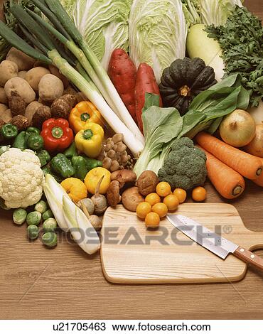 Stock Image - Large assortment of vegetables with a cutting board and knife. Fotosearch