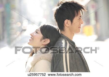 Stock Image - Portrait of young couple standing back to back. Fotosearch