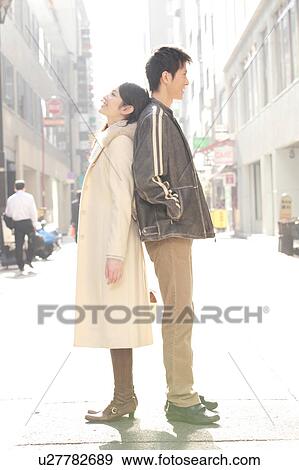 Stock Photo - Portrait of young couple standing back to back on the street. Fotosearch