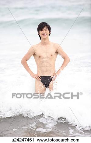 Stock Image - Portrait of young man in swimsuit in surf at the beach. Fotosearch