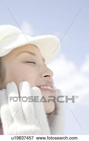 Stock Photo - Portrait of young woman with hat and gloves to her face. Fotosearch