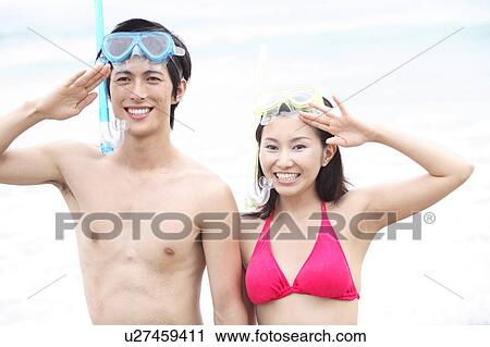 Stock Image - Young couple in swimsuits at the beach saluting. Fotosearch