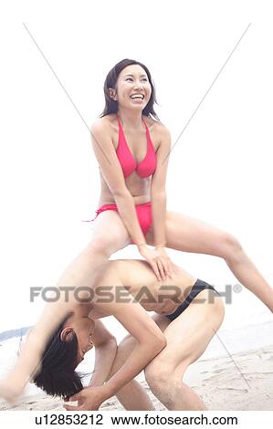 Stock Image - Young couple in swimsuits playing leapfrog at the beach. Fotosearch