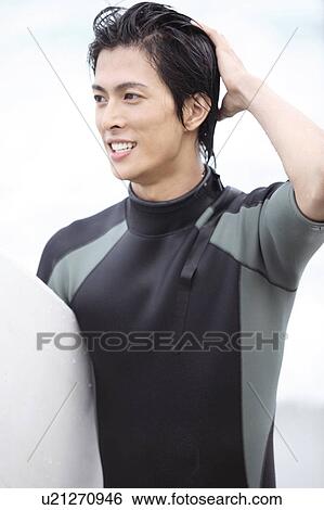 Stock Photograph - Young surfer at the beach wearing wet suit. Fotosearch