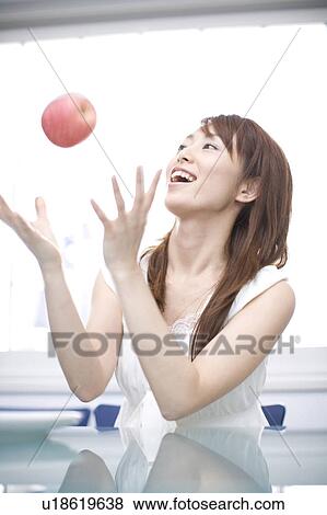 Stock Photo - Young woman laughing and tossing an apple. Fotosearch