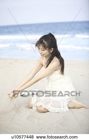 Stock Photo - Young Woman scooping the sand on the beach. Fotosearch