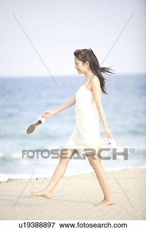 Stock Photo - Young woman walking along the beach. Fotosearch