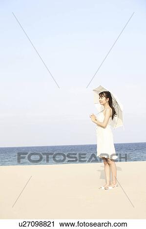 Stock Image - Young woman with umbrella on the beach. Fotosearch