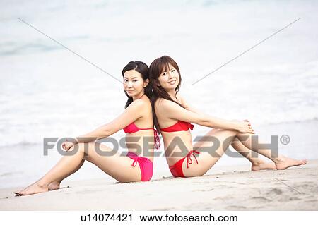 Stock Image - Young women in swimsuits sitting on the beach. Fotosearch