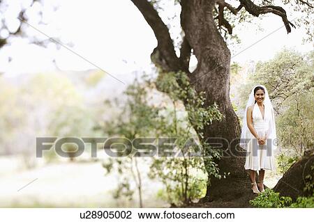 Stock Image - Bride standing under a tree and smiling. Fotosearch