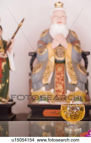 Picture - Close-up of a candle burning in front of a figurine of Confucius. Fotosearch