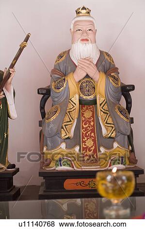 Stock Photo - Close-up of a candle burning in front of a figurine of Confucius. Fotosearch