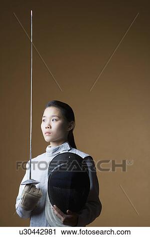Stock Image - Close-up of a female fencer holding a sword and a fencing mask. Fotosearch